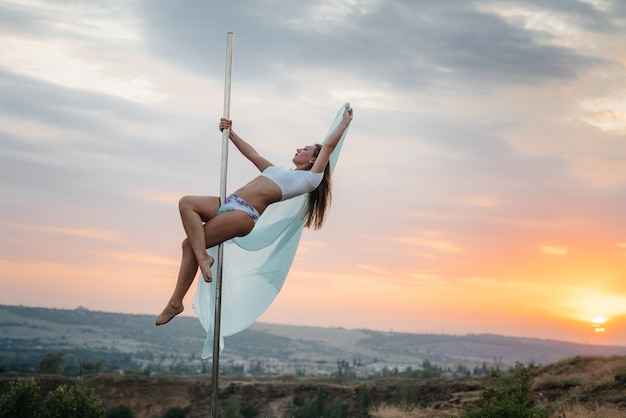 A young sexy girl performs amazing exercises on a pole during a beautiful sunset. Dance. Sexuality.