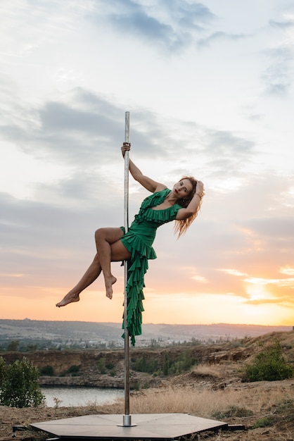 A young sexy girl performs amazing exercises on a pole during a beautiful sunset. Dance. Sexuality.