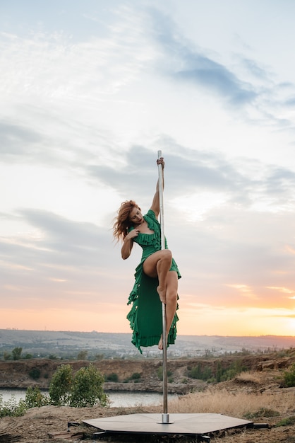 Una giovane ragazza sexy esegue incredibili esercizi su un palo durante un bellissimo tramonto. danza. sessualità.