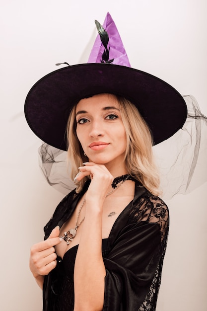 Young sexy girl in a witch hat touches her face with her hand