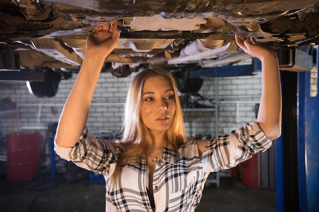 写真 横を向いて車の修理サービスで車の下に立っている若いセクシーなメカニック女性
