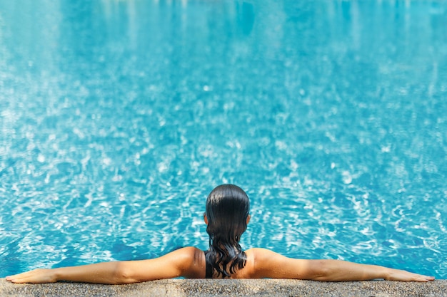 夏の暑い日にクリスタルブルーの水でトロピカルスイミングプールでリラックスした若いセクシーなスリムな女性