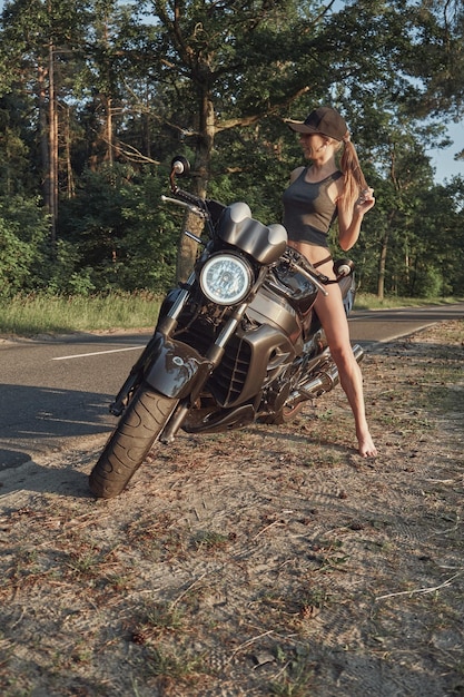 Young sexy woman biker in bikini sitting on a motorcycle on the side of a forest road