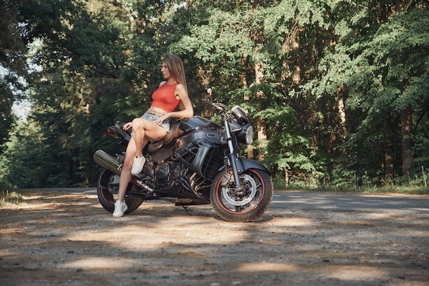 Young sexy woman biker sitting on a motorcycle on the side of a forest road