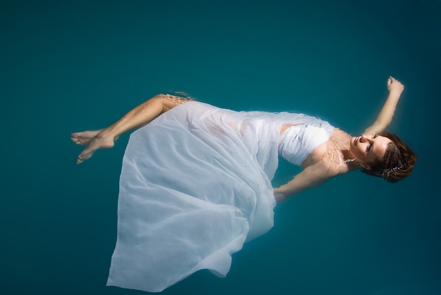 Young sexy woman floating on swimming pool in white dress. beauty shot