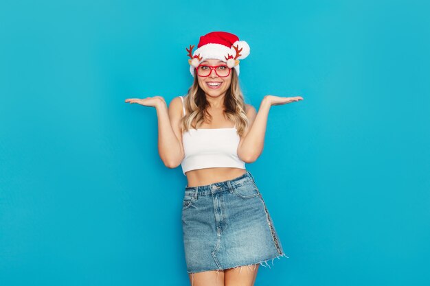 A young sexy woman in a short top denim skirt Santa hat Christmas glasse spreads hands with doubt