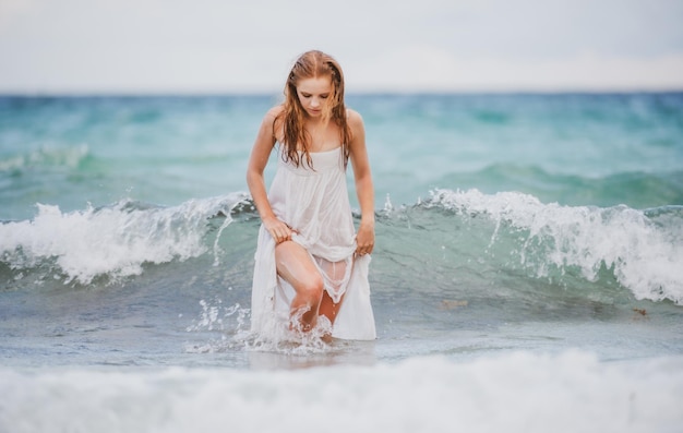 Young sexy woman at waves sea summer beach sensual girl girl in white dress on tropical beach vacation