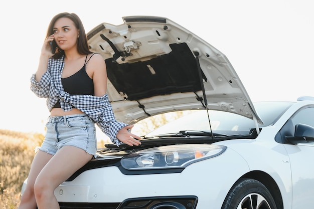 壊れた車を持ったセクシーな若い女性が携帯電話で電話しています