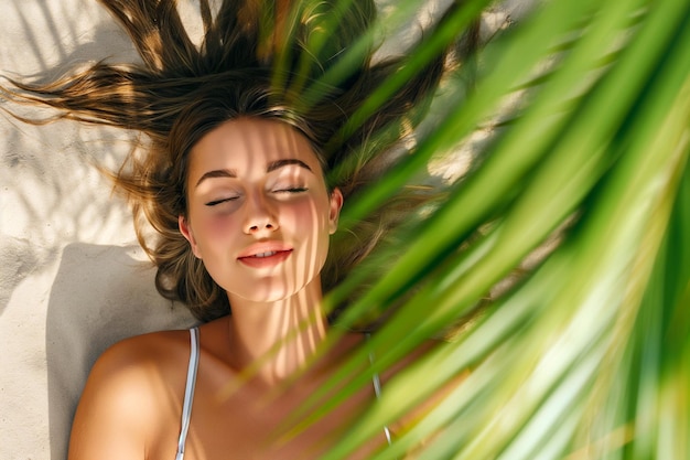 Photo young sexy woman with closed eyes lying under a palm tree woman sunbathes in a shadow under palm tree branches relaxation on the sand beach at summer vacation tanned skin slim body