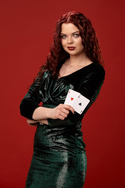 Young sexy woman with a red curly hair holding aces, on a red background. Poker