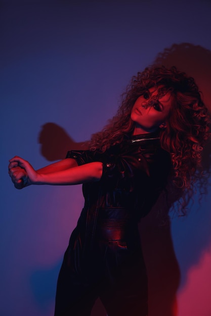 Young and sexy woman with a stylish Afro hairstyle wearing leather biker suit posing in colorful neon light