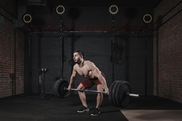 写真 crossfit ジムで重いバーベルを持ち上げる若い上半身裸のアスリート