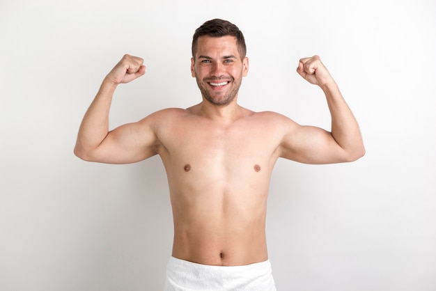 young shirtless man flexing his muscles against white wall