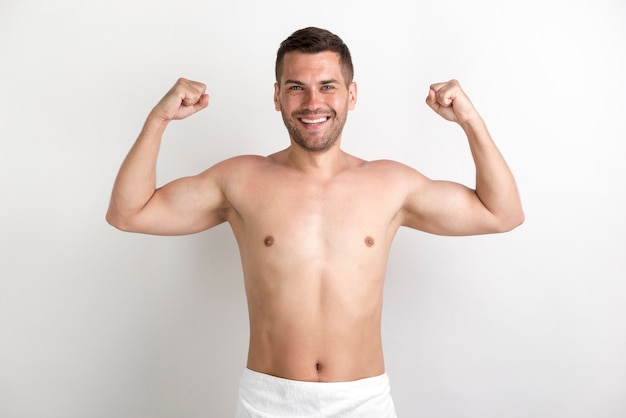 Photo young shirtless man flexing his muscles against white wall