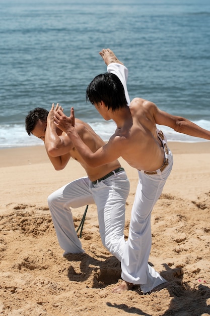 Foto giovani uomini senza camicia che praticano la capoeira insieme sulla spiaggia