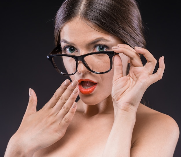 Giovane donna senza camicia in bicchieri con rossetto rosso sulle labbra.