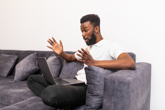 Young shocked black man chatting online on laptop with friend at home.  