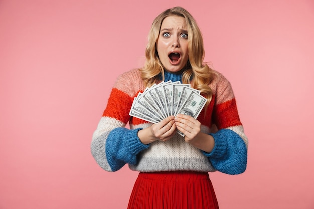 young shocked pretty beautiful woman posing isolated over pink wall holding money