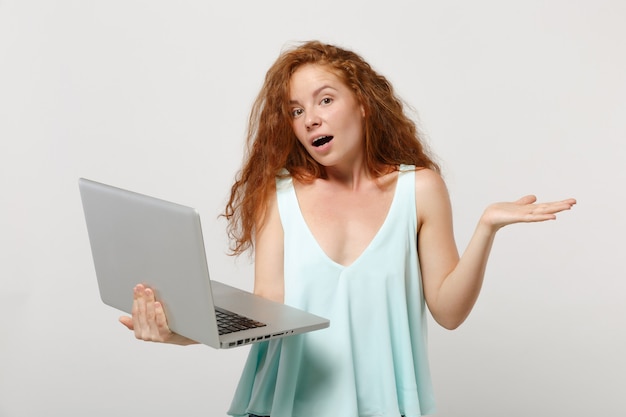 Ragazza giovane donna rossa scioccata in abiti casual leggeri in posa isolata su sfondo bianco in studio. concetto di stile di vita della gente. mock up copia spazio. lavorando su un computer portatile, allargando le mani.