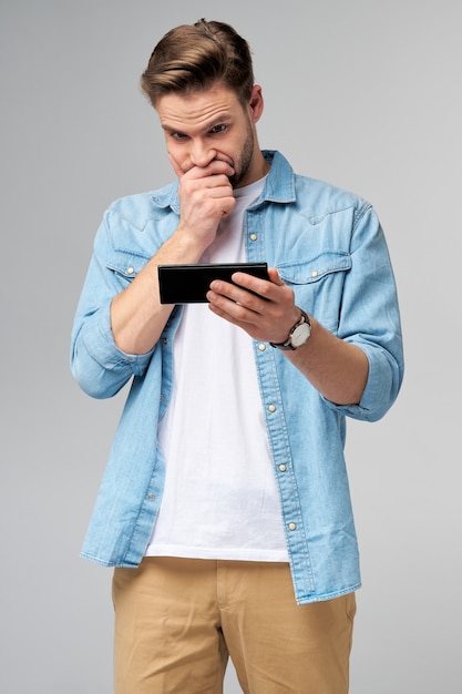 Young shocked stressed angry and frustrated man using smartphone