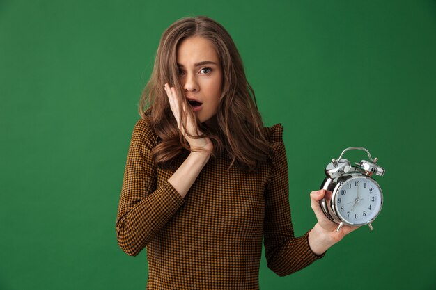 Young shocked woman holding alarm clock.