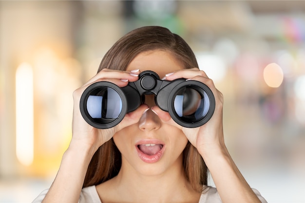 Young shocked woman with binoculars on blurred background