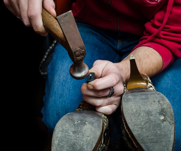 Young shoemaker repairing a old pair of shoes heel with a tool hamer