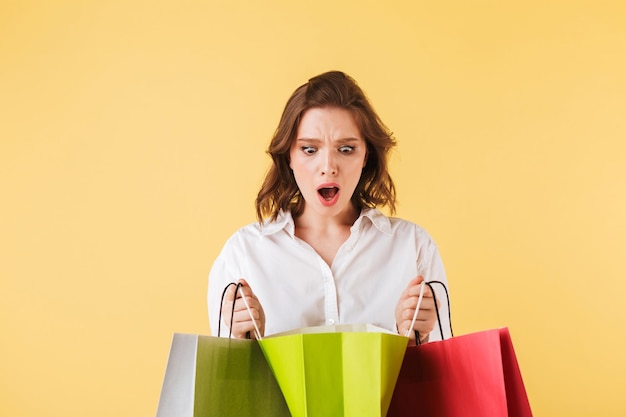 Young shoked lady standing and amazedly looking in colorful shopping bags in hands on over colorful background