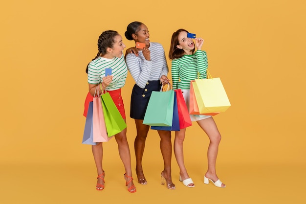 Young shopping multiethnic ladies use credit card hold shopping bags