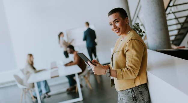 オフィスに立って、彼女のチームの前でデジタルタブレットを使用して若いショートヘアのビジネスウーマン