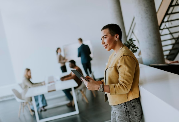 Young short hair business woman standing in the office and using digital tablet in front of her team