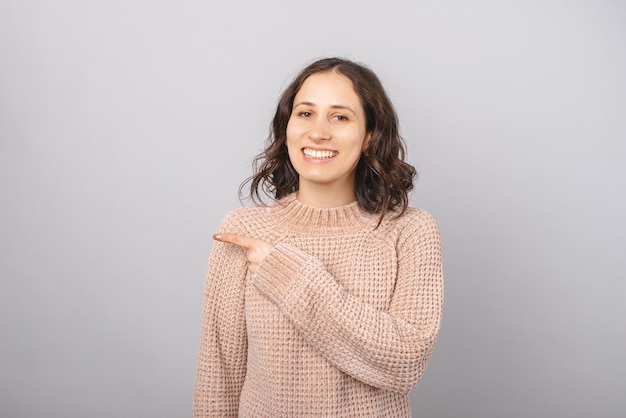 Young short hair smiling woman is pointing aside over grey background