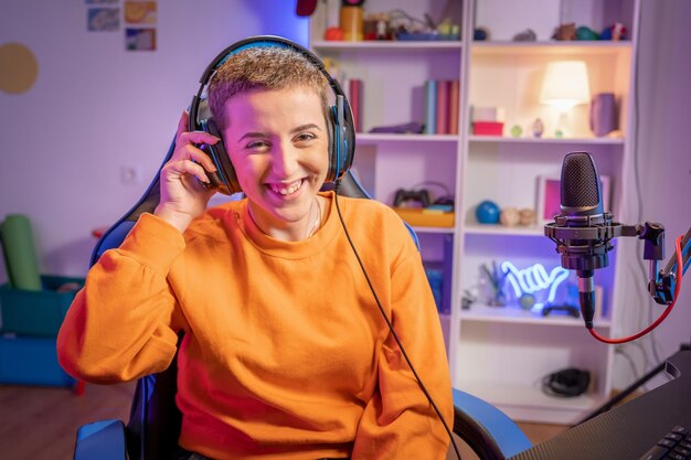 Young short haircut woman gamer playing video games wearing headphones smiling looking at camera