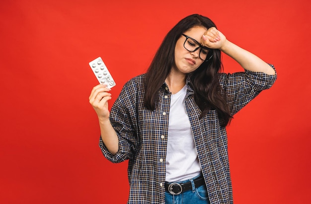 赤い背景の上に隔離された食事の丸薬を保持している若い病気または風邪の女性インフルエンザ風邪の概念