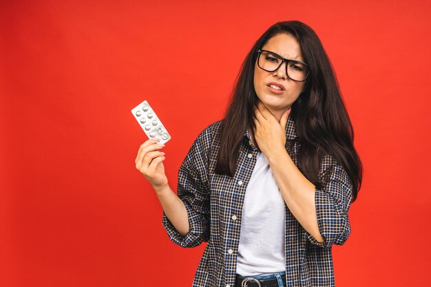 赤い背景の上に隔離された食事の丸薬を保持している若い病気または風邪の女性インフルエンザ風邪の概念