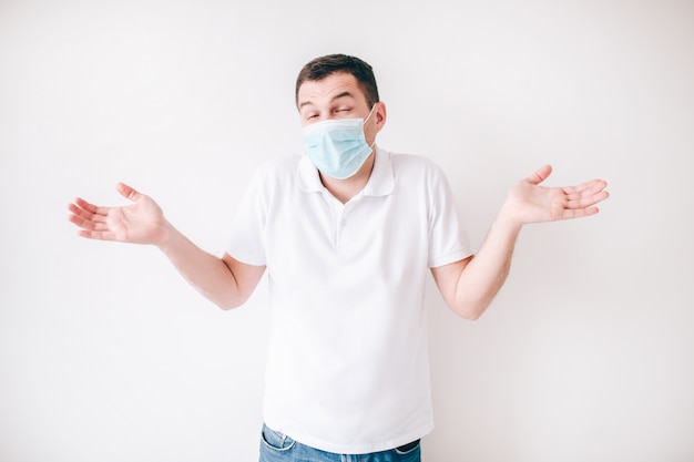 Young sick man isolated over white wall. Confused guy wonder. Hold hands aside body. Wear facial protection mask.