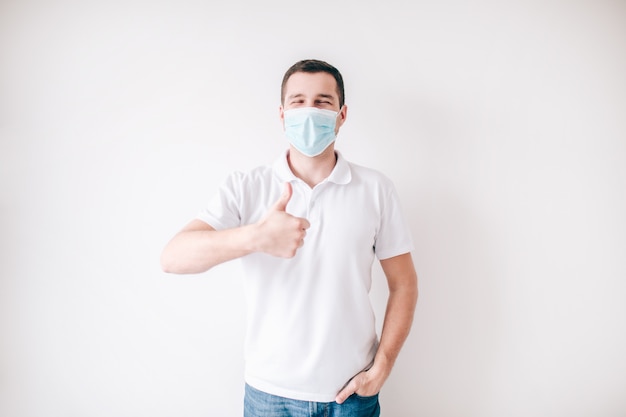 Young sick man isolated over white wall. Guy in medical mask hold big thumb up. Protection from virus and flu.