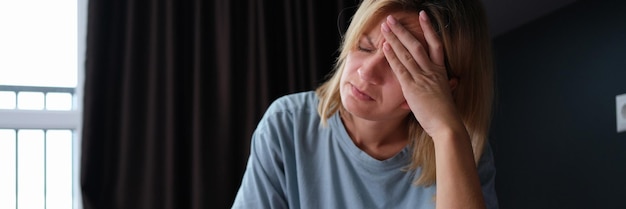 Young sick woman in pajamas sitting in bed and holding her head