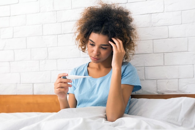 Young sick woman with fever checking her temperature