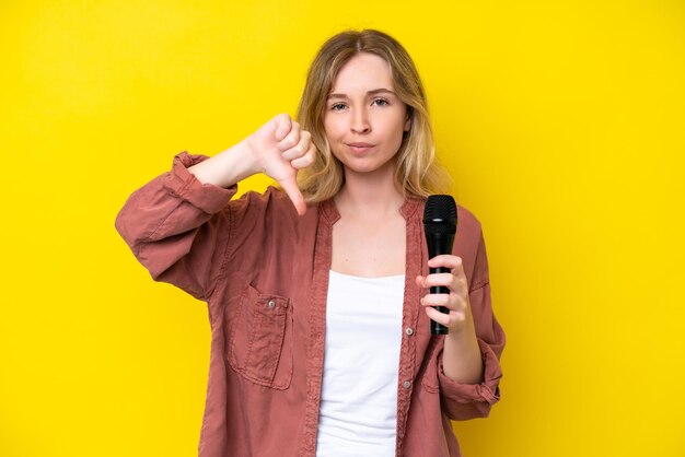 Photo young singer caucasian woman picking up a microphone isolated on yellow background showing thumb down with negative expression