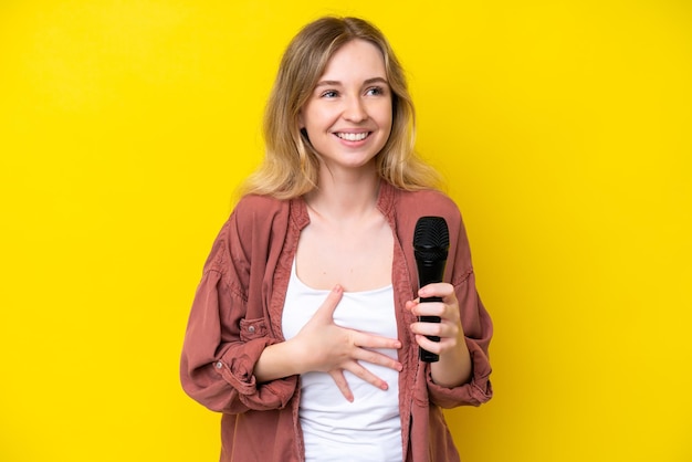 Giovane cantante donna caucasica che prende in mano un microfono isolato su sfondo giallo che sorride molto