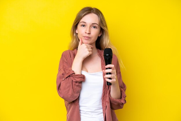 Young singer caucasian woman picking up a microphone isolated on yellow background thinking