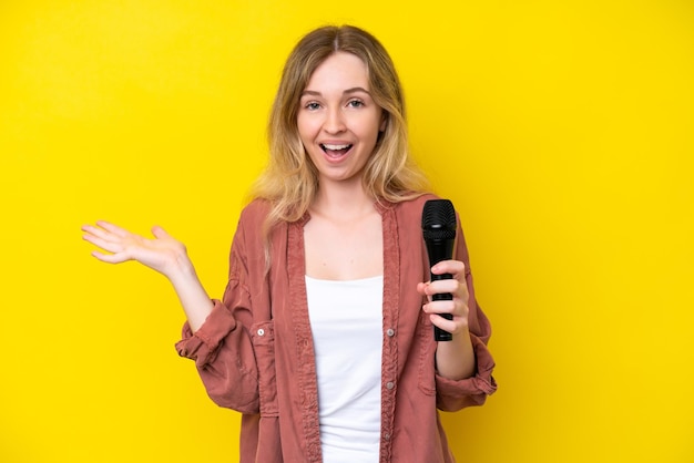 Young singer caucasian woman picking up a microphone isolated on yellow background with shocked facial expression