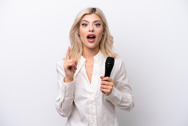 Young singer woman picking up a microphone isolated on white background intending to realizes the solution while lifting a finger up