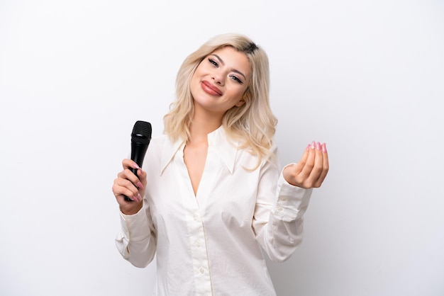 Young singer woman picking up a microphone isolated on white background making money gesture