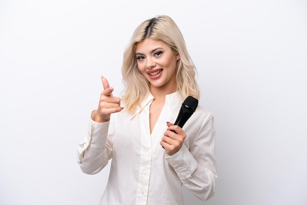 Young singer woman picking up a microphone isolated on white background pointing front with happy expression