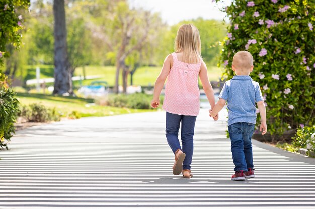 Photo young sister and brother holding hands and walking at the park