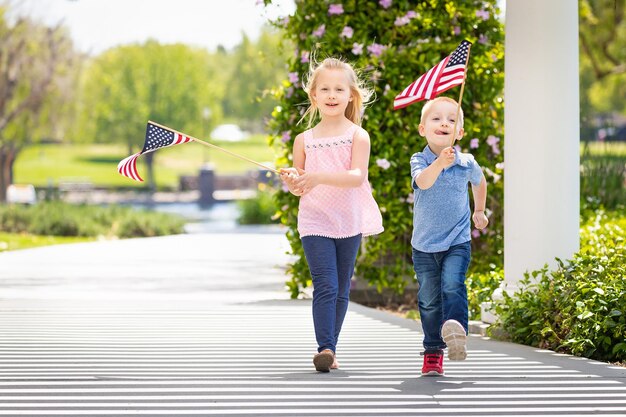 Photo young sister and brother waving american flags at the park