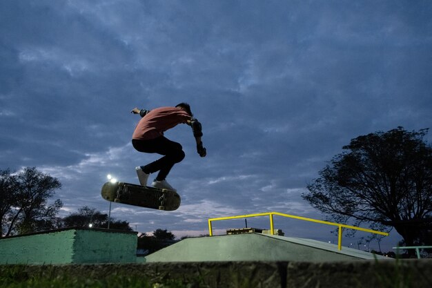 Foto giovane skateboarder che fa un trucco nello skatepark durante la notte