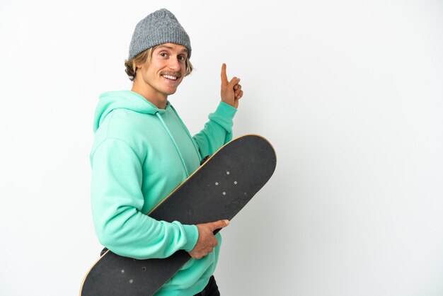 Young skater blonde man isolated on white wall pointing back